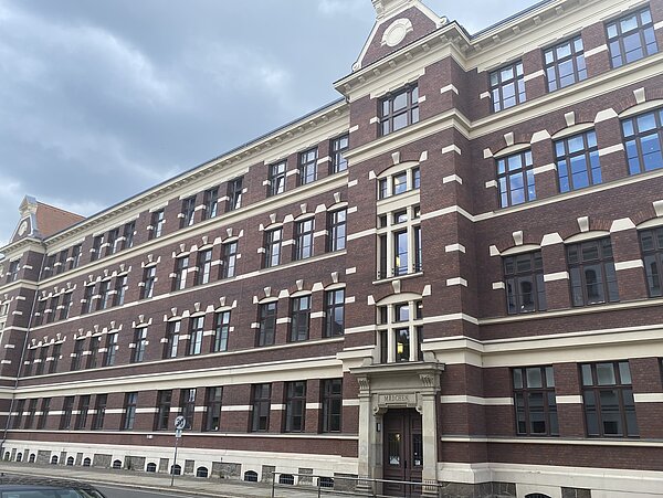 Das Bild zeigt einen brauen Backsteingebäudekomplex mit weißen Verziehrungen. 