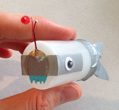 Selbstgebauter Fisch aus Dose und Diode zwischen zwei Fingern